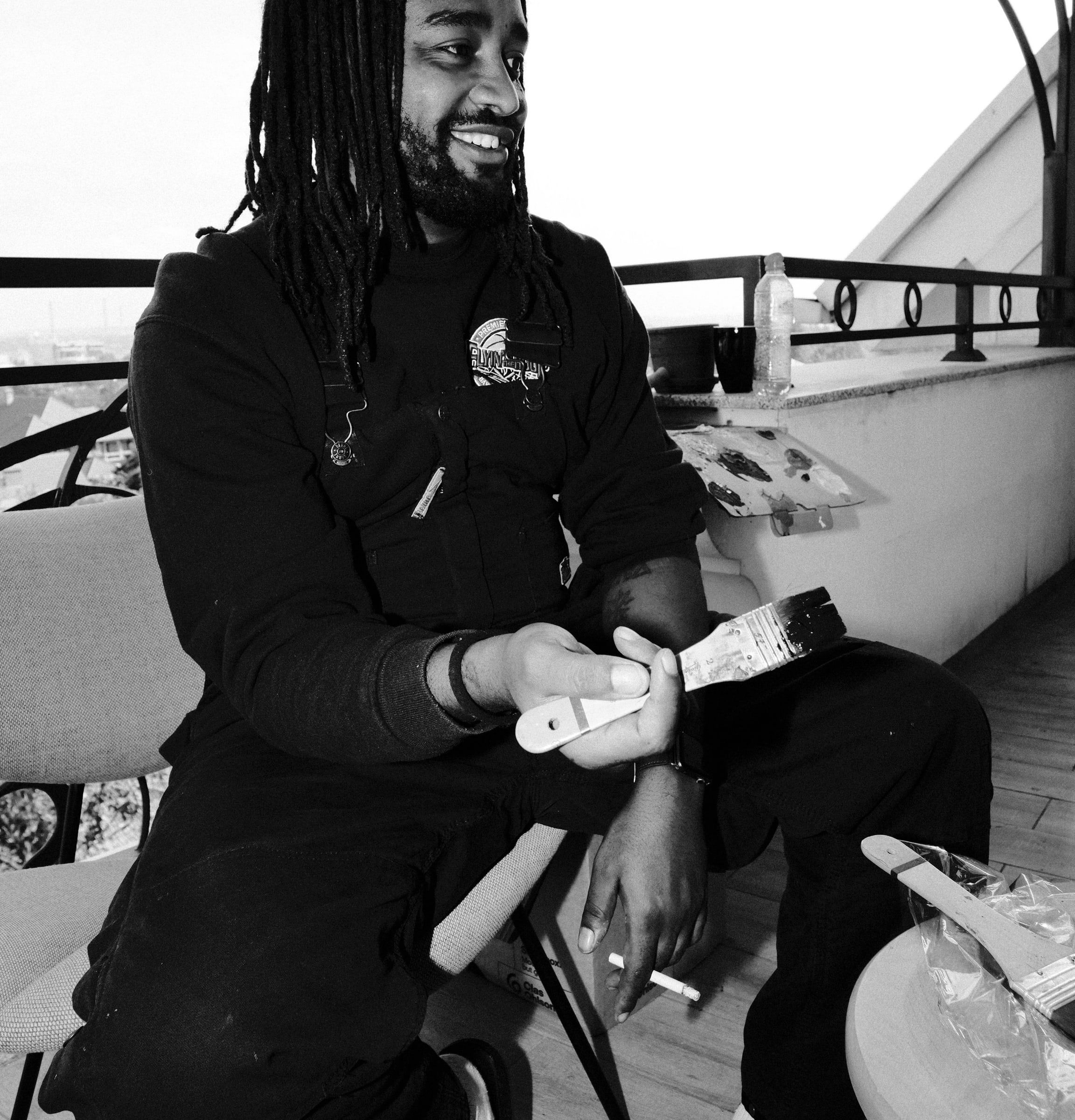 Dawit smiling on a balcony, holding a wide brush, in black and white