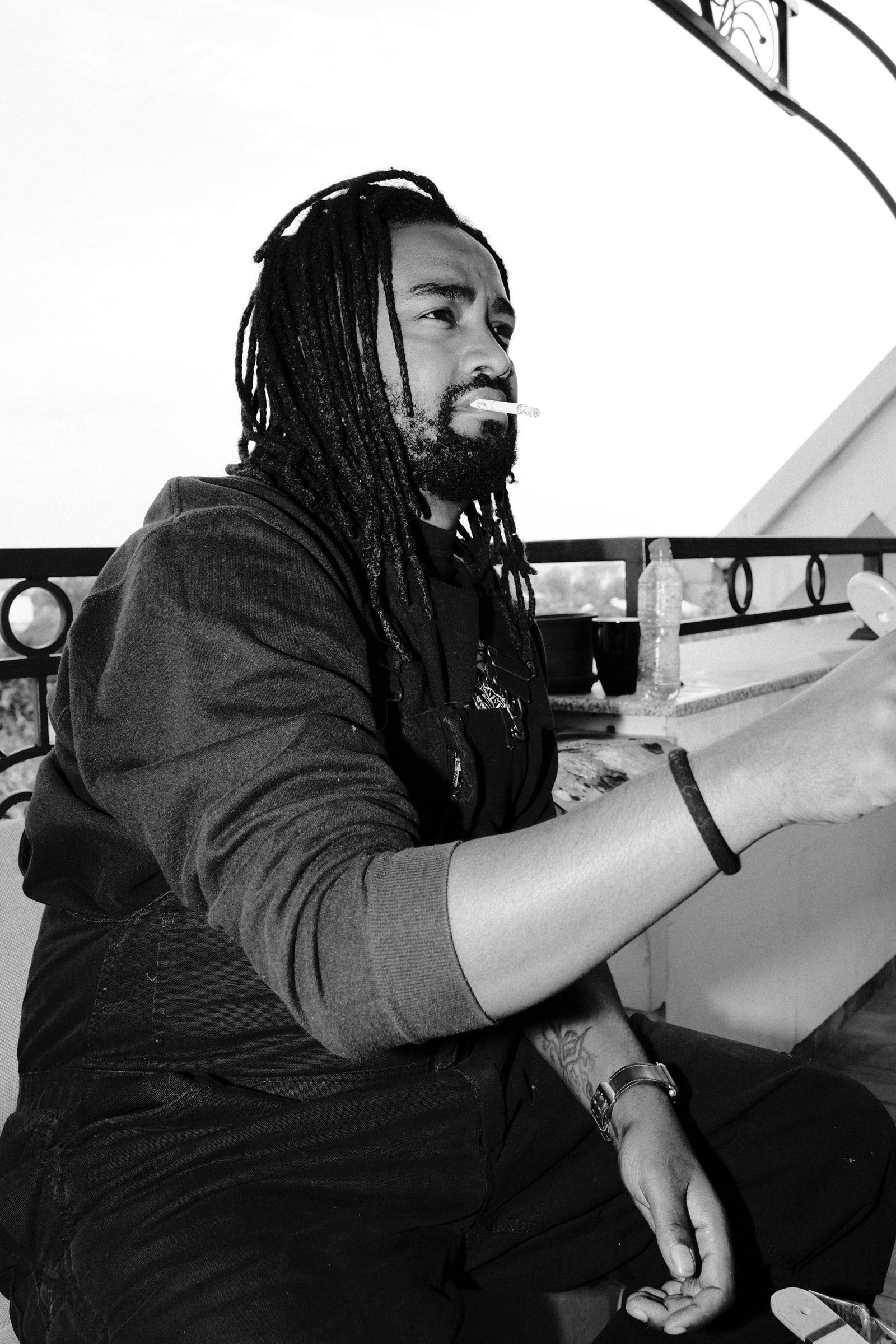 Dawit sitting on the balcony with a cigarette, looking to the side, in black and white