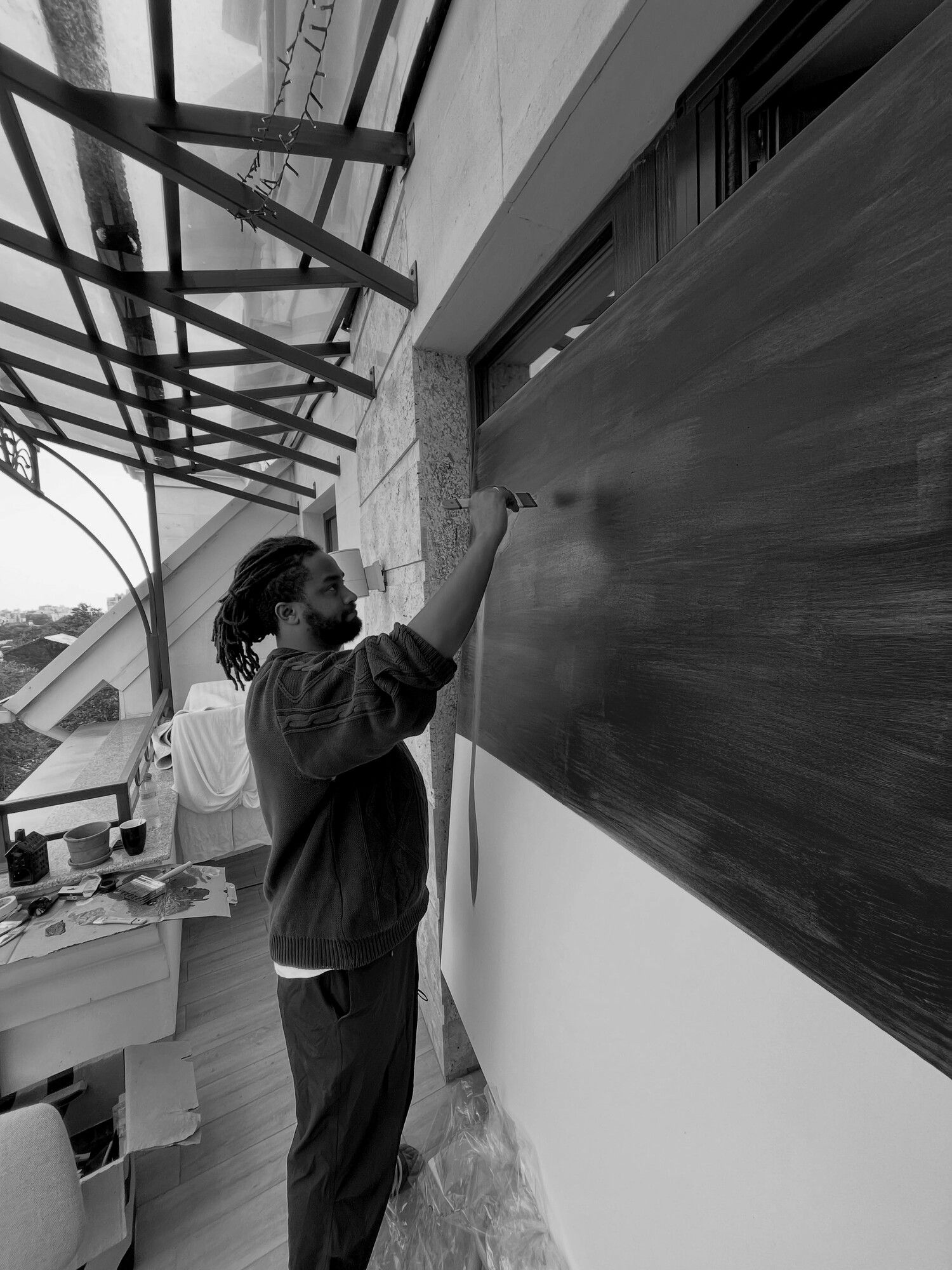 Dawit painting the magenta ground of My sunflower on a balcony, in black and white